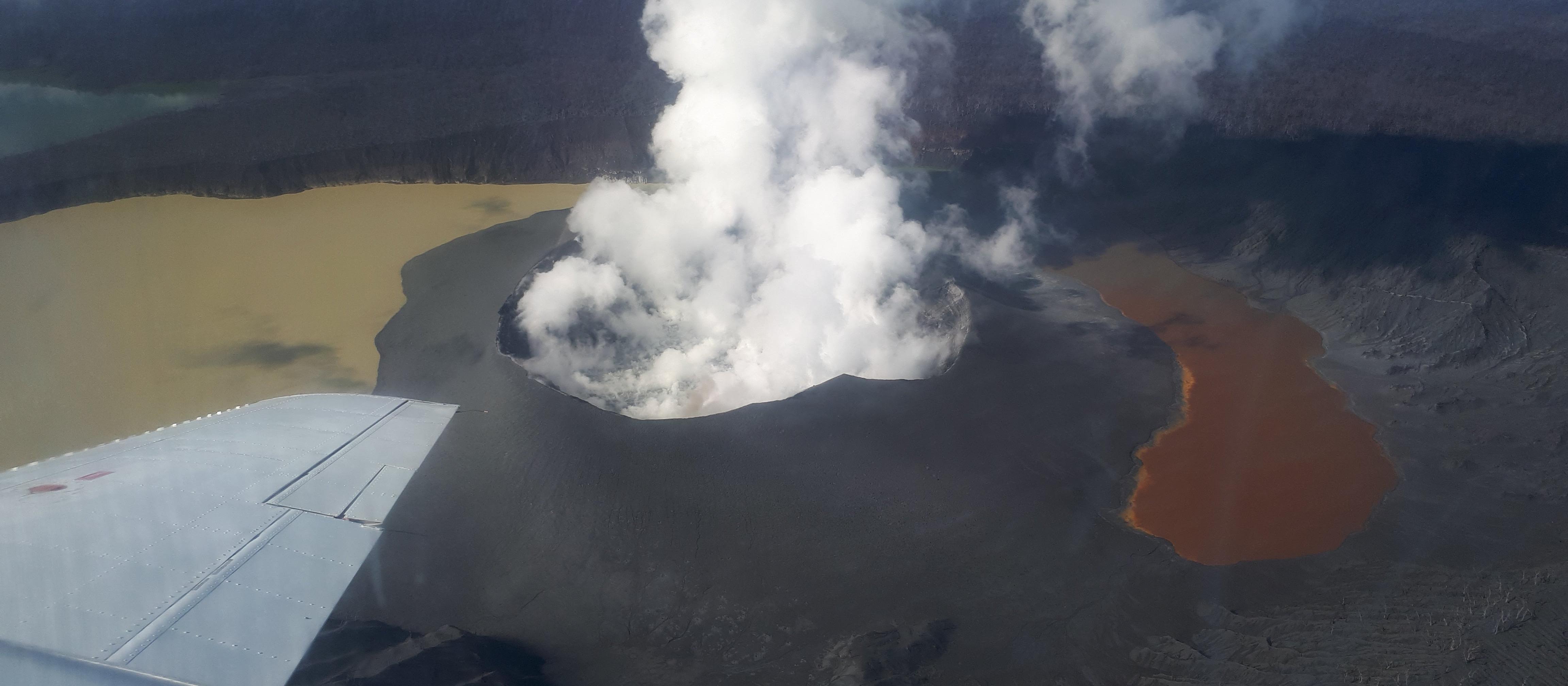 Ambae volcano and Lake Voui on 21 April 2018, Ambae Island, Vanuatu. The lake has been split into two due to the growth of the new volcanic cone. The visible landscape is covered with thick ash deposits. The dead trees in the lower right were killed over a decade ago during another eruptive episode. Photo credit: Natalia Deligne.