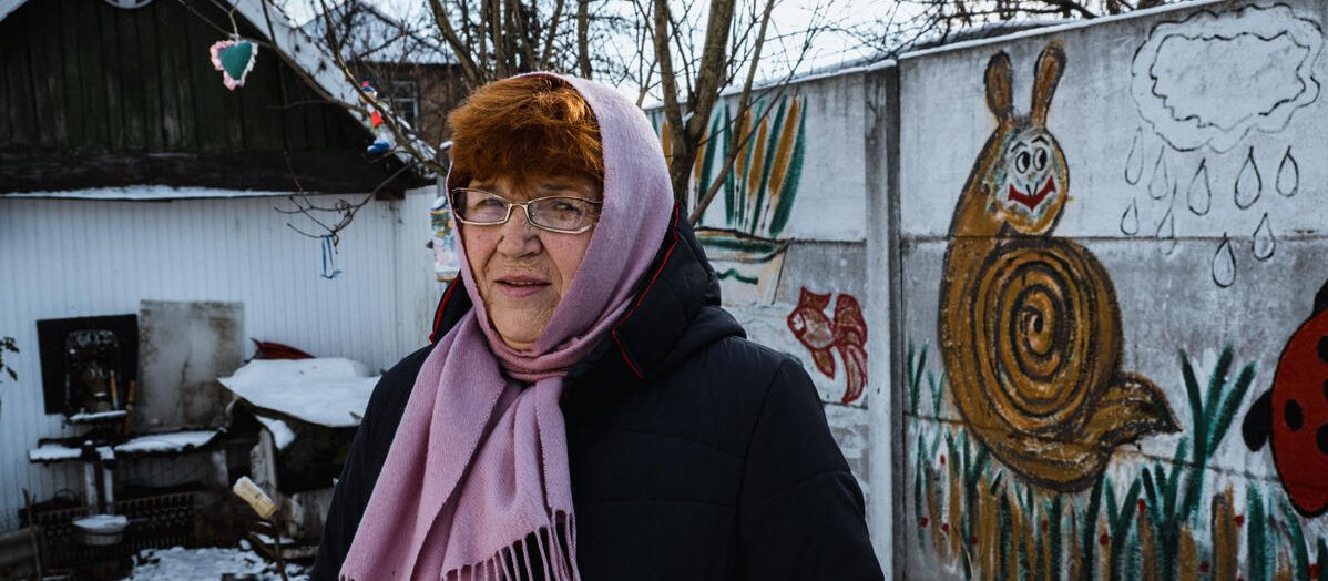 68-year-old grandmother, Larysa-, standing in the yard of her house in Ukraine in front of a wall that she painted [Image: Olena Dudchenko/Save the Children]