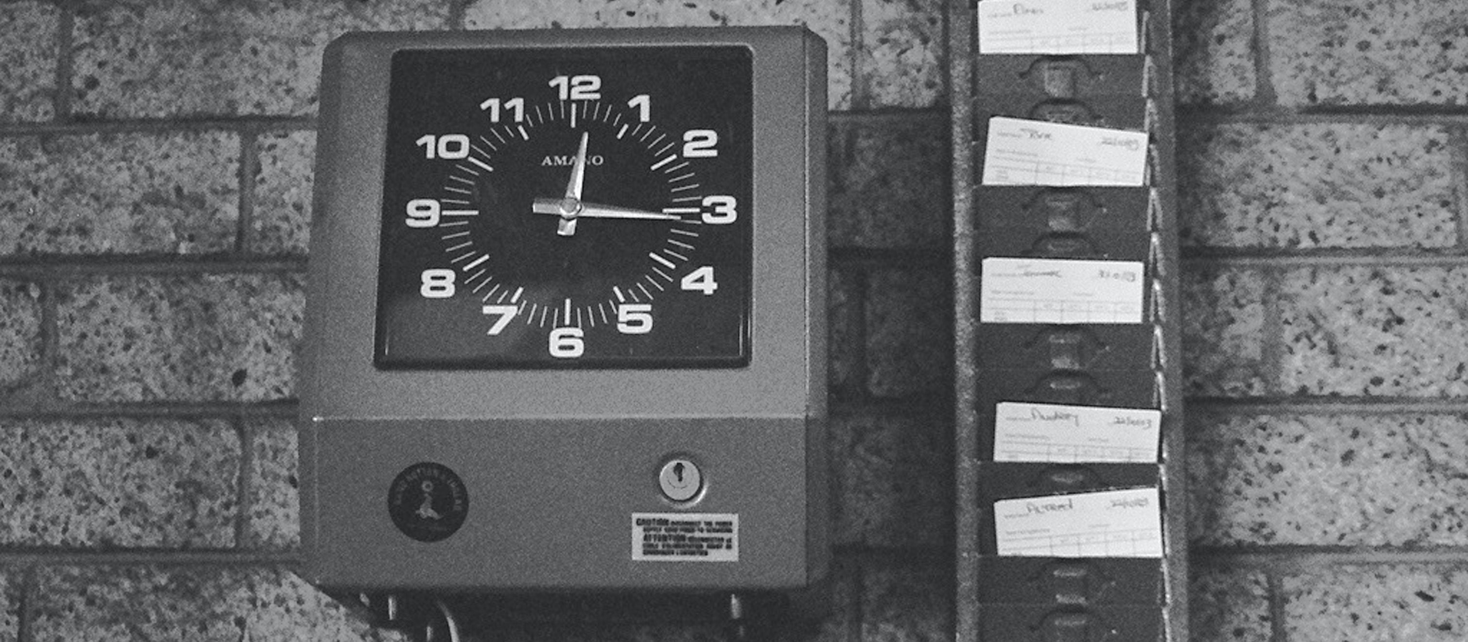 Image in black and white shows an employee time card machine beside a row of time cards