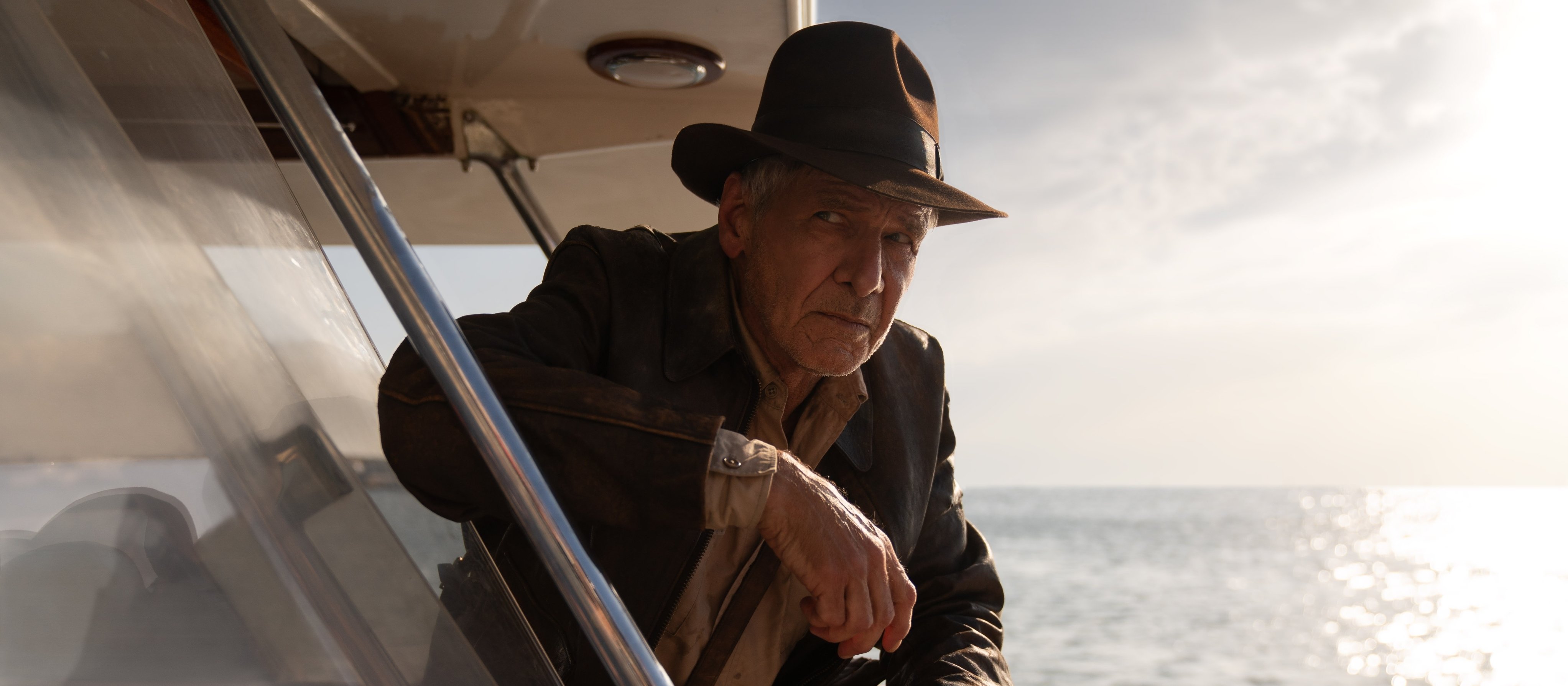 Older man in fedora on yacht overlooking glistening ocean