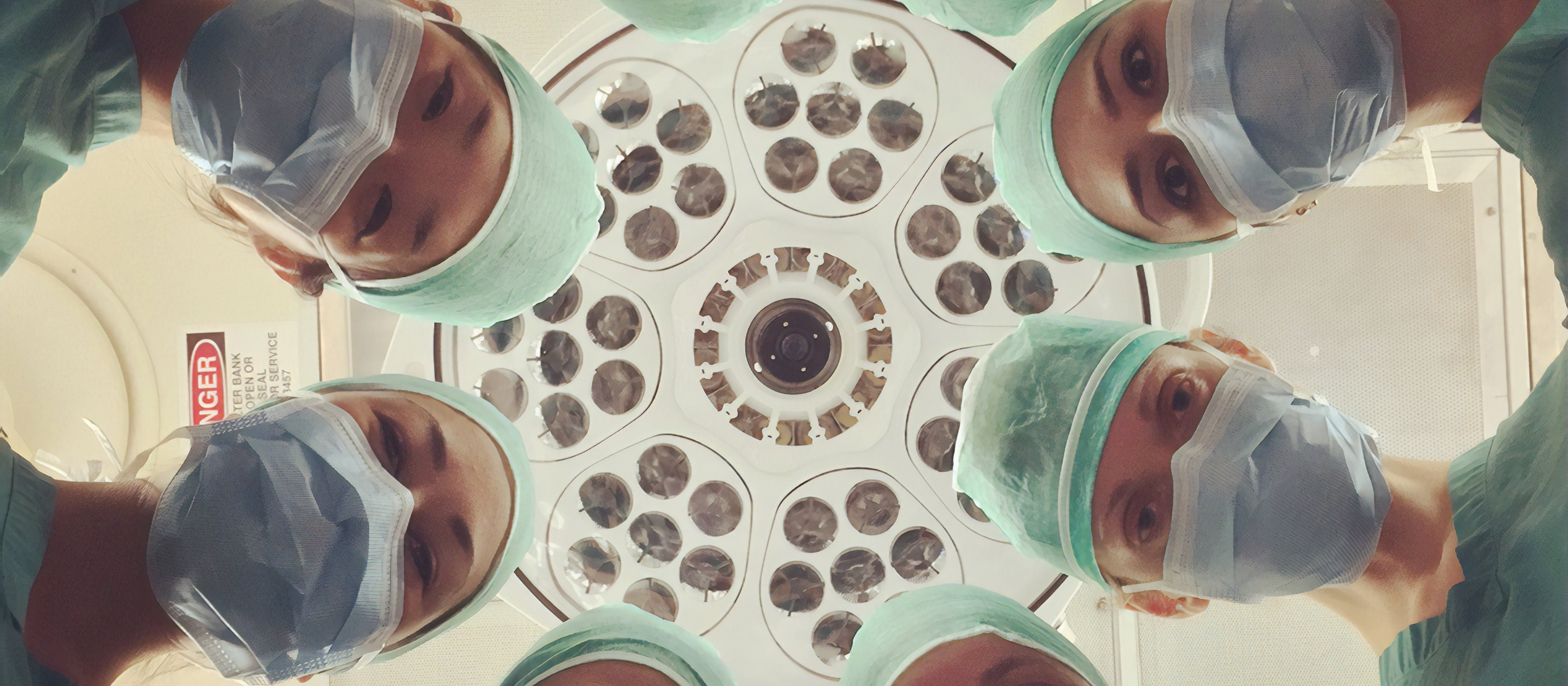 Faces of surgeons wearing masks and standing in a circle looking down