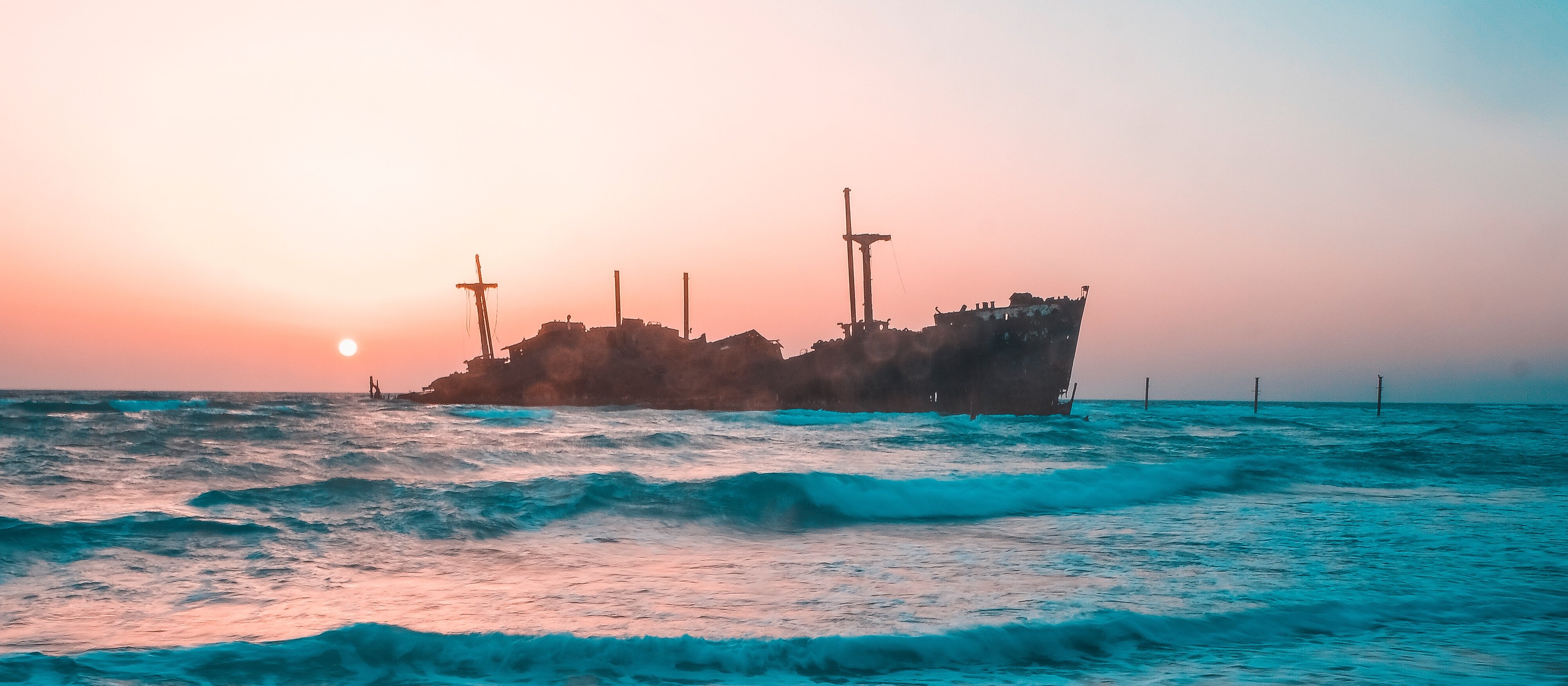 A beach with a ship sinking in background