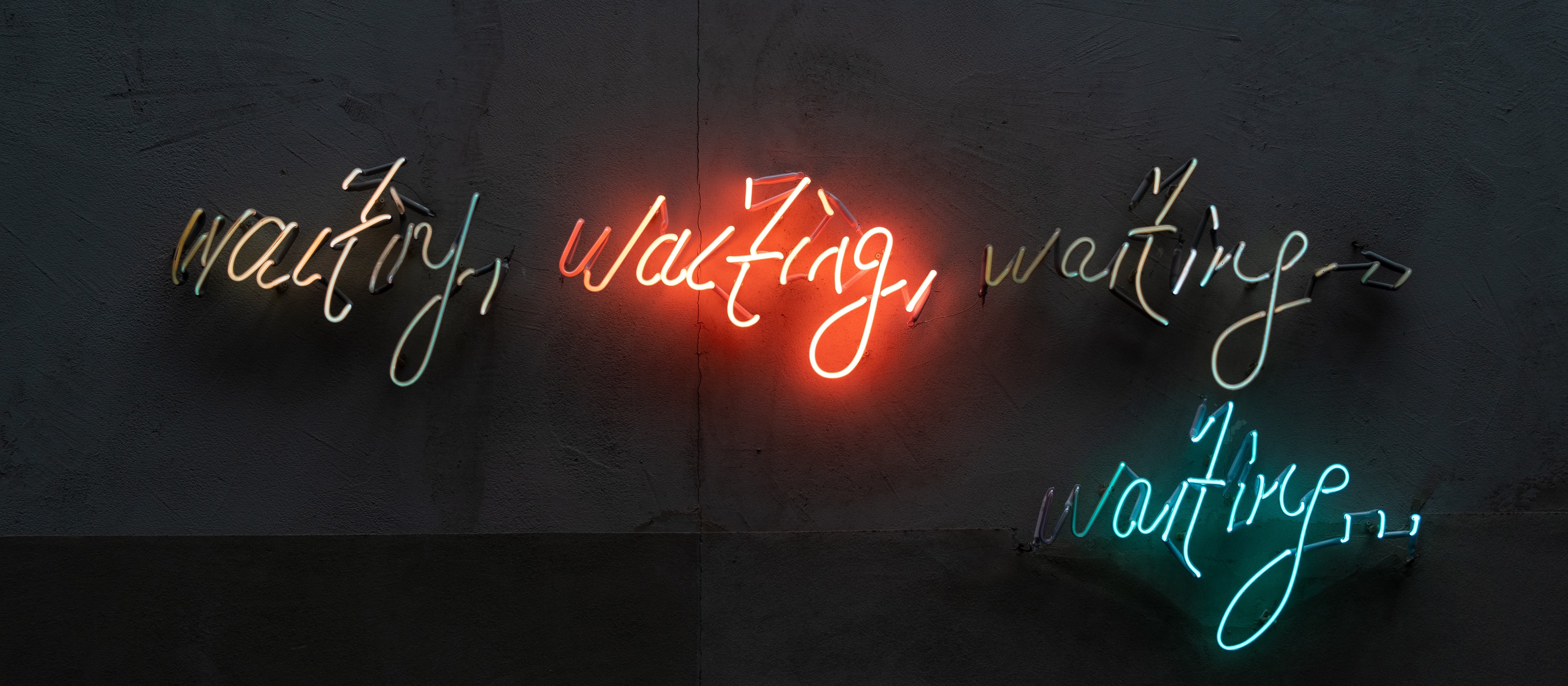 Neon lights on a black background read: waiting, waiting, waiting