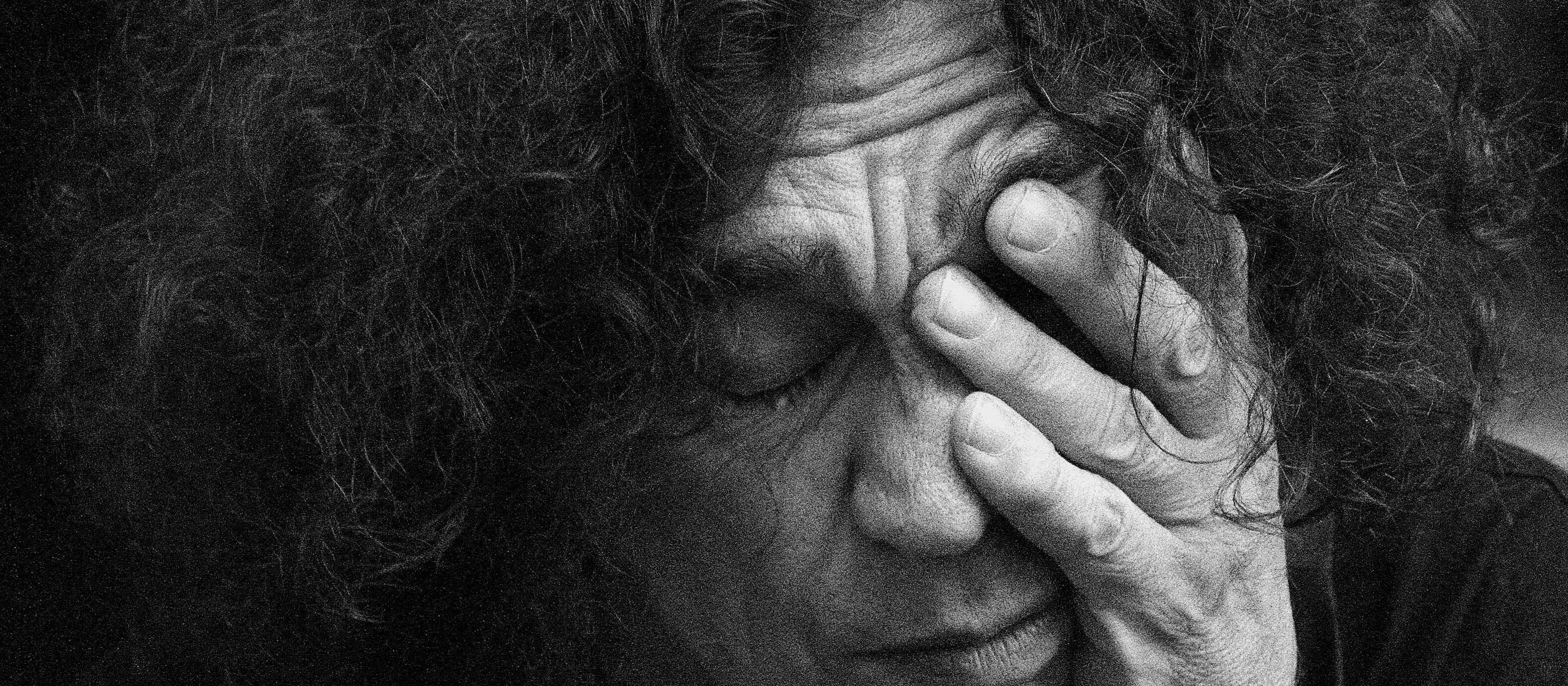 Black and white image showing person with curly heai rubbing their face with one hand