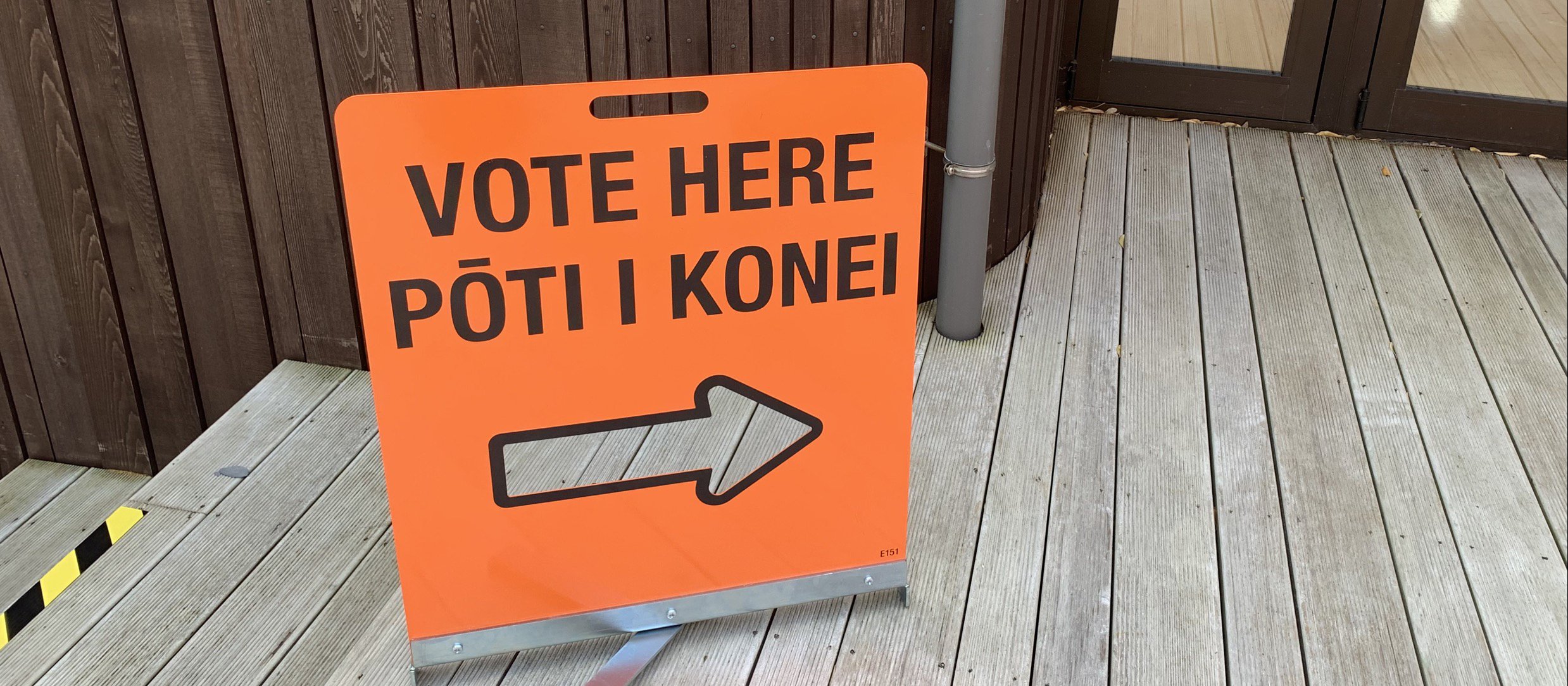 An orange sign reads 'vote here pōti i konei' with a clear cut arrow pointing to a door on the right