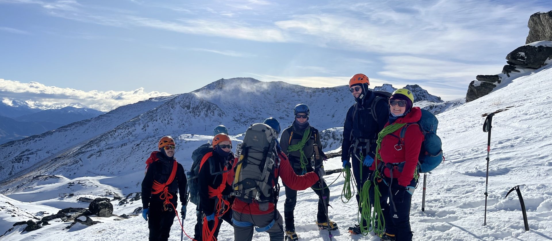 Photo shows group of people in mountaineering gear standing on a snowy mountain