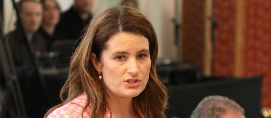 Woman with brown hair in pink check blazer, talking