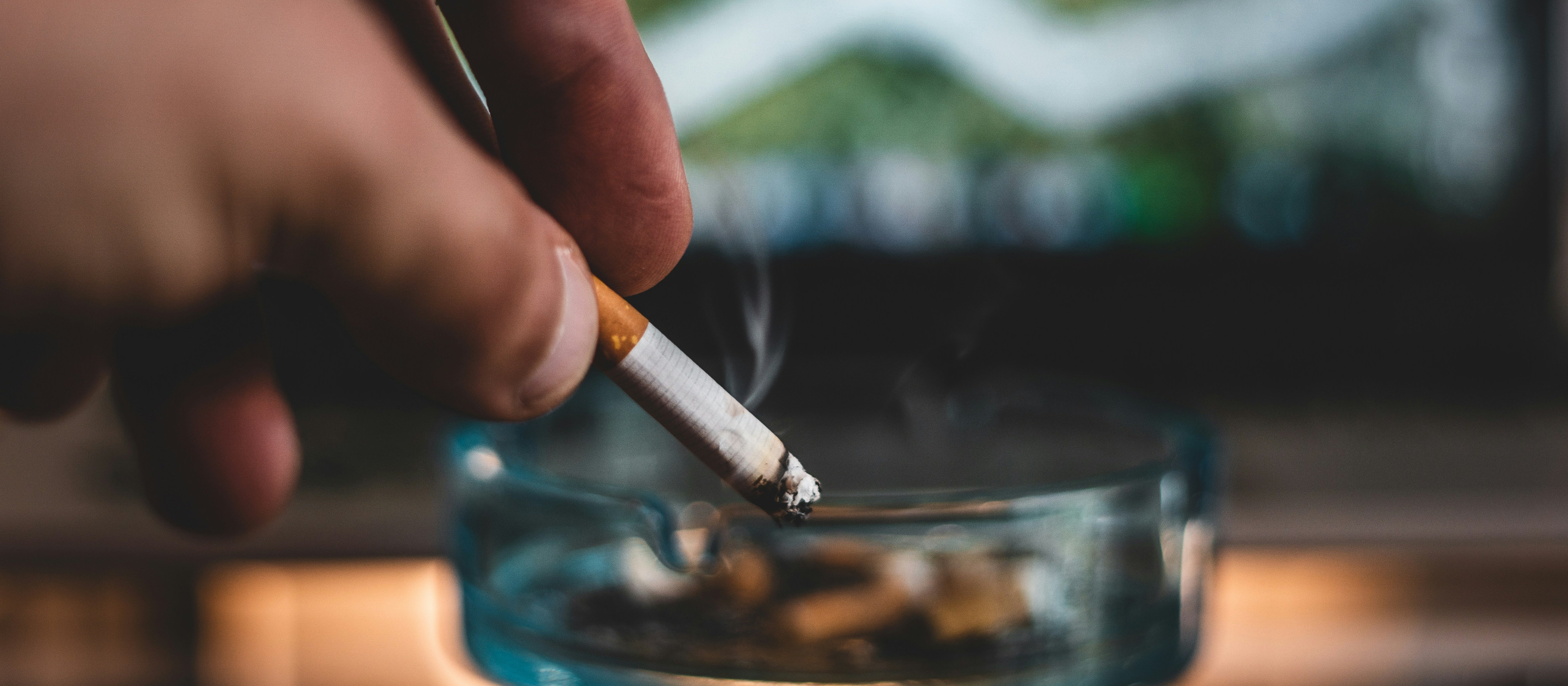 A hand holding a lit cigarette towards an ashtray