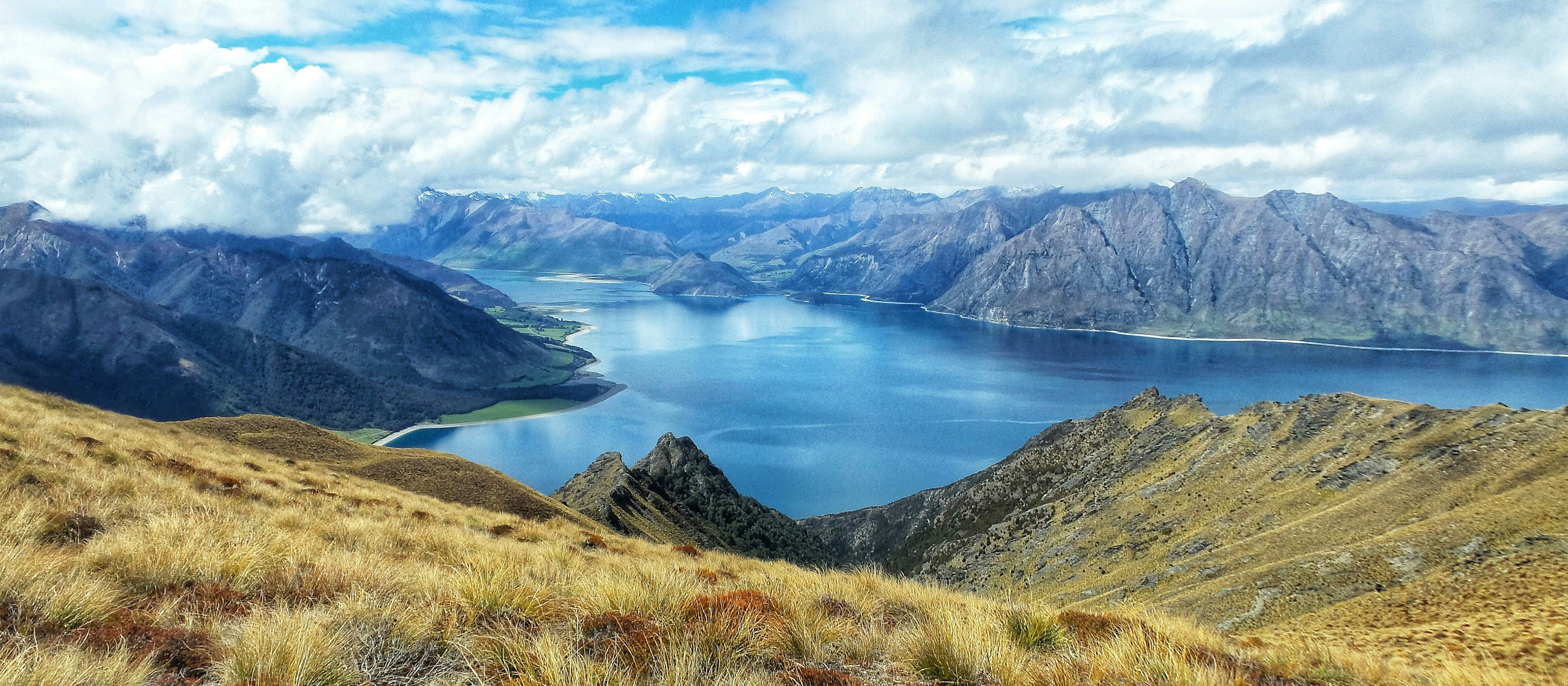 Grassy hills above a lake surrounded by mountains, clouds in a blue sky