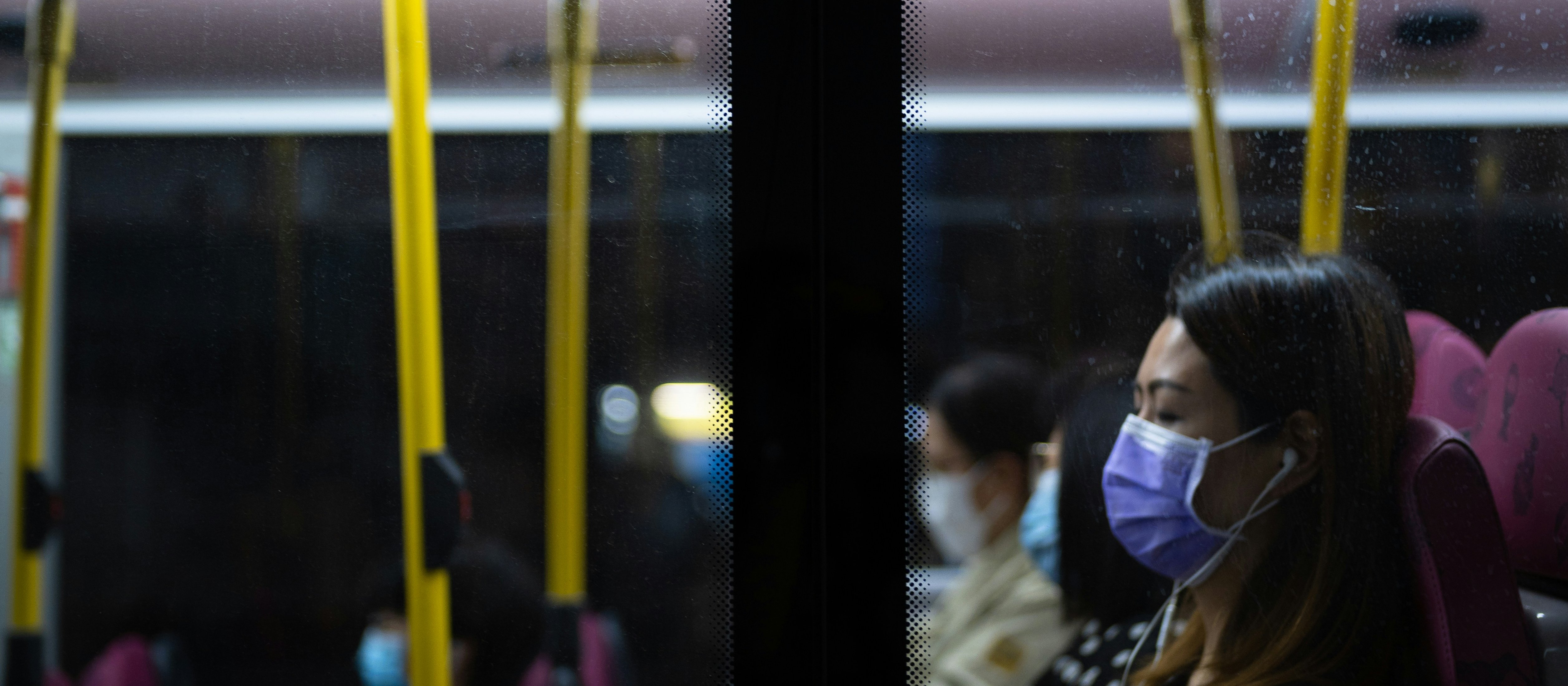Woman with dark hair wears a mask on a bus
