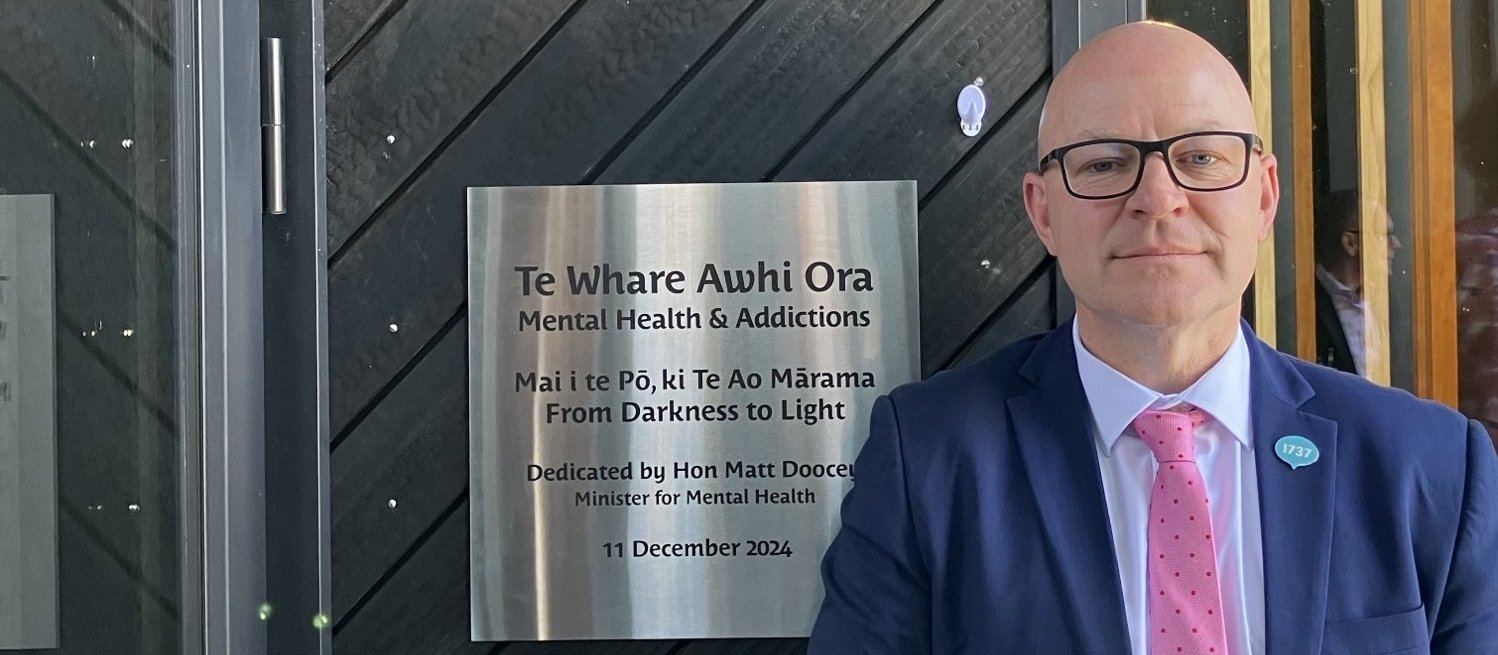 Matt Doocey, in navy suit and pink tie, standing beside a plaque marking the opening of a new mental health unit at Gisborne hospital