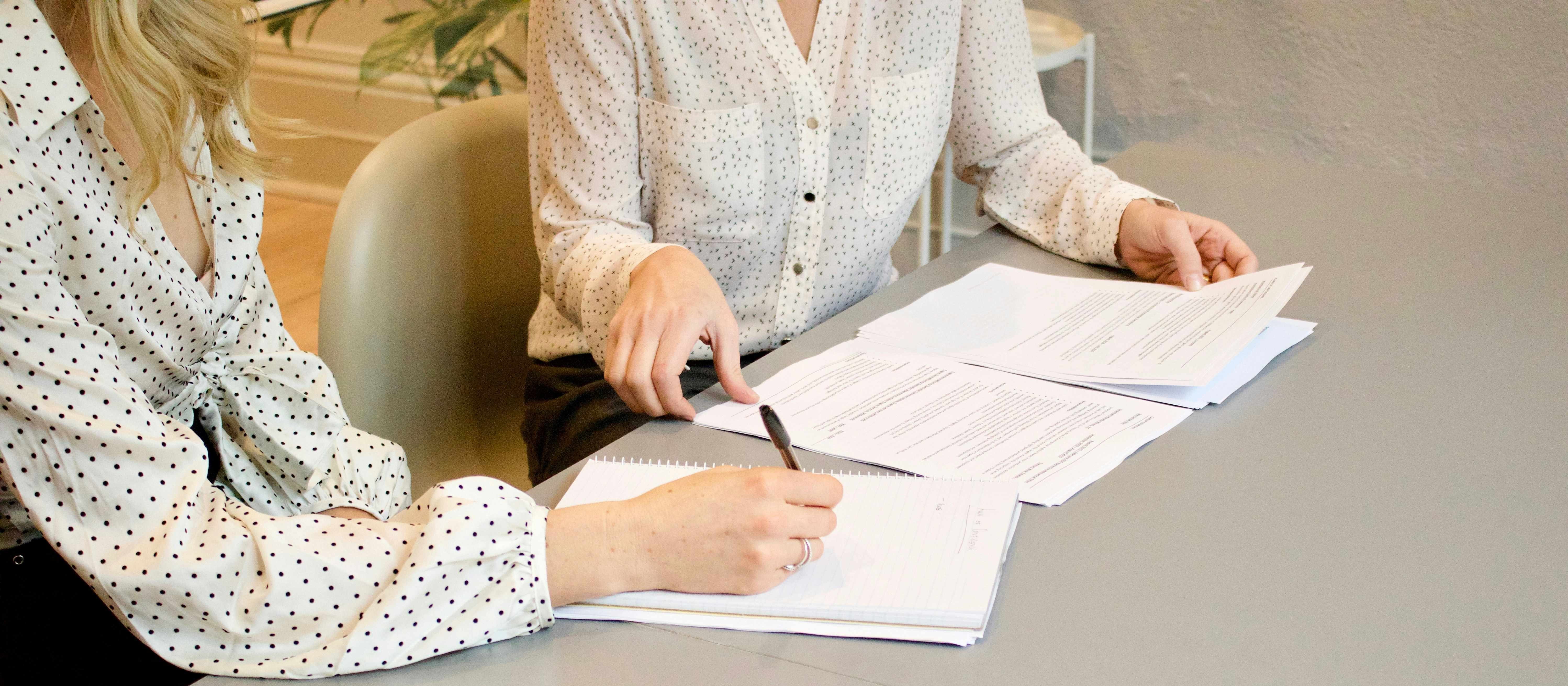 Two women in white blouses sitting at a table with paperwork