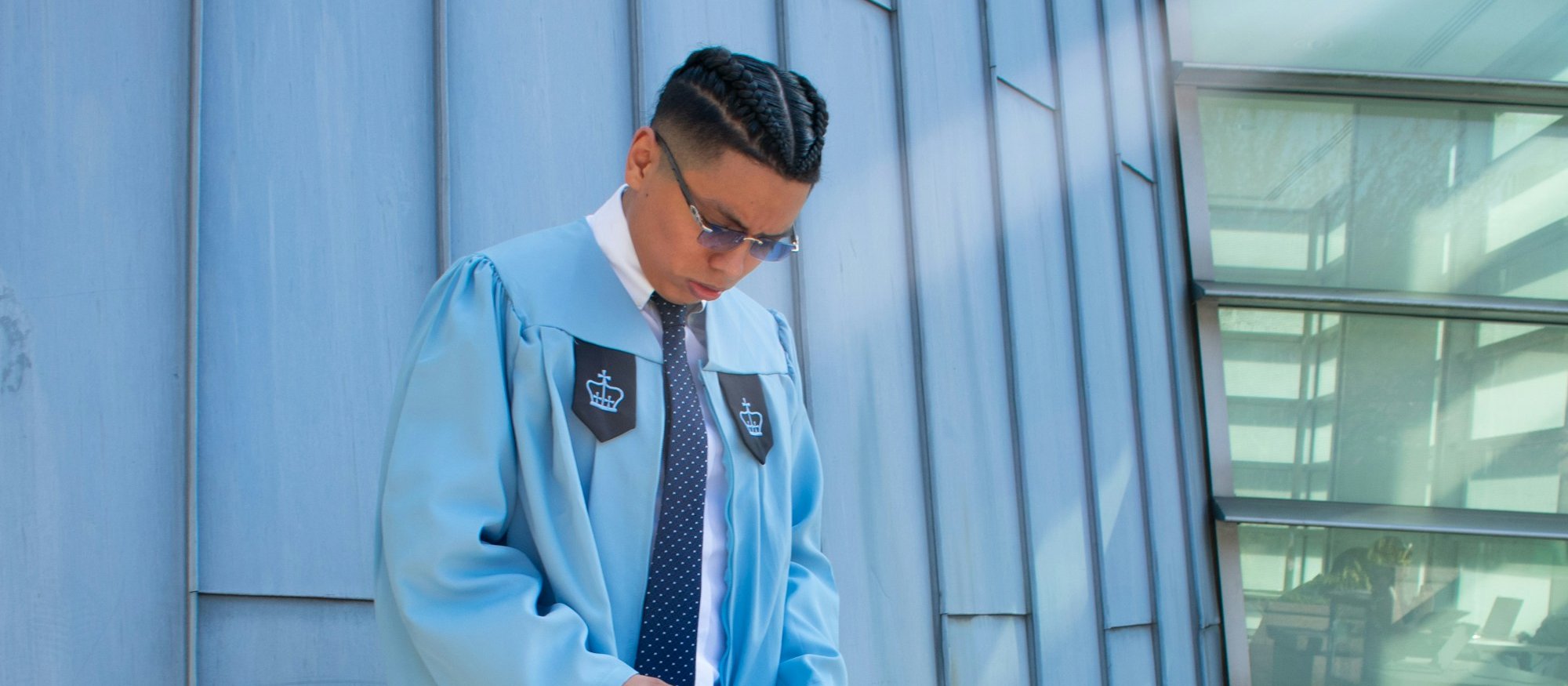 Man in light blue graduation gown holding mortarboard cap