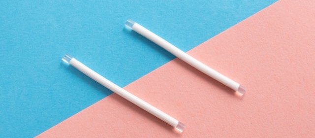 Two white contraceptive implant rods on a pink and blue background