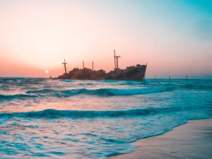 A beach with a ship sinking in background