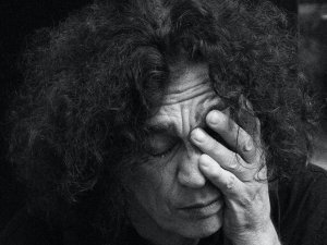 Black and white image showing person with curly heai rubbing their face with one hand