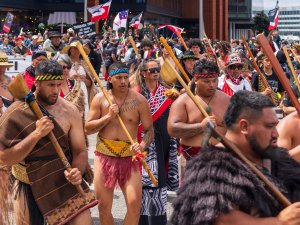 Māori men in traditional clothing at the head of the hikoi to Parliament, behind them other protestors carry flags