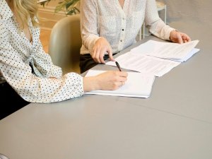 Two women in white blouses sitting at a table with paperwork