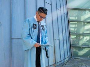 Man in light blue graduation gown holding mortarboard cap