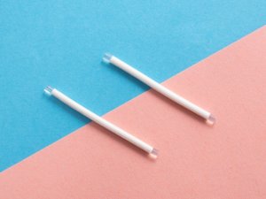 Two white contraceptive implant rods on a pink and blue background