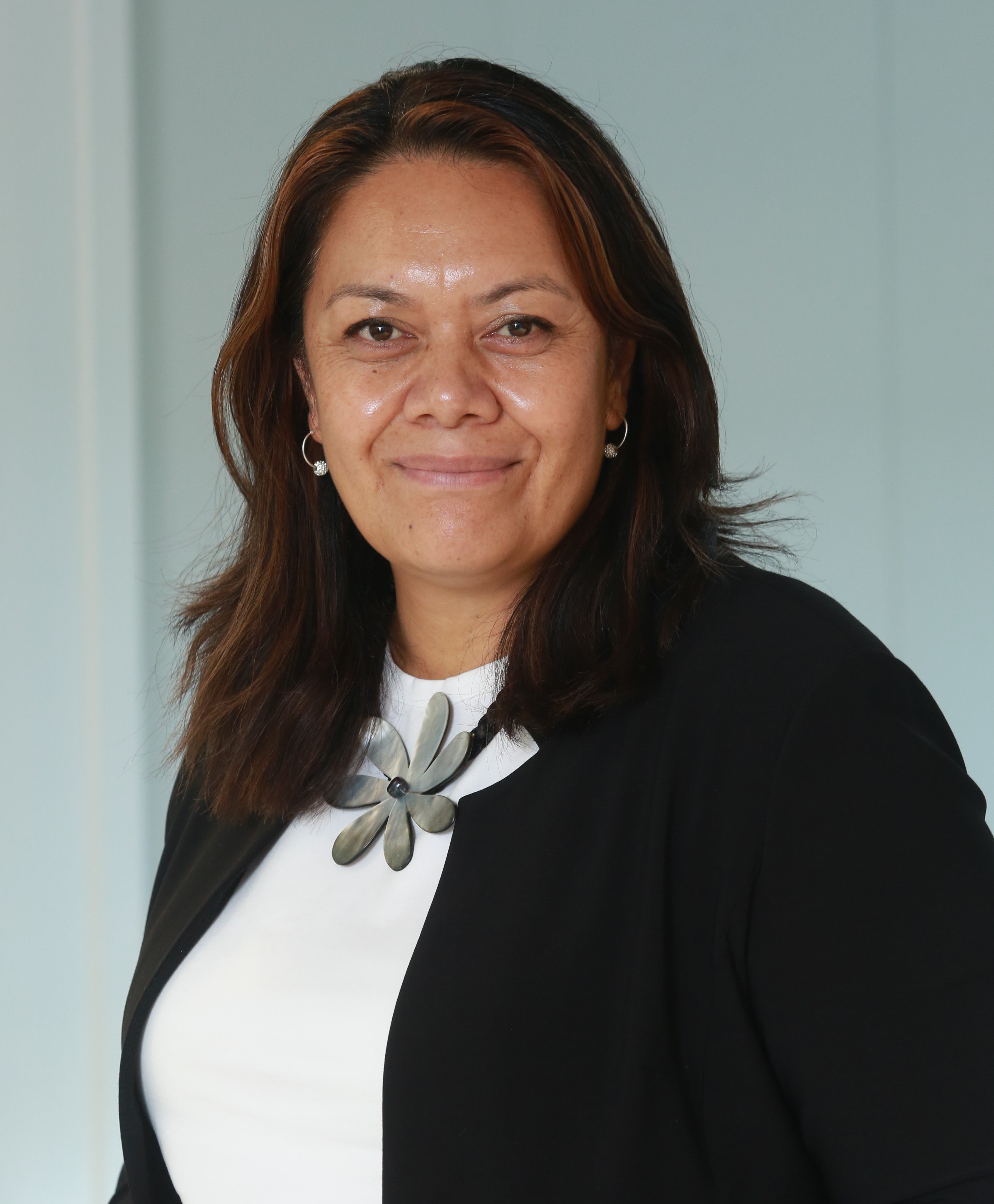 Margie Apa, wearing a white top with a flower and black blazer, smiling at camera