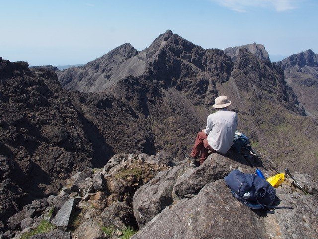 A man sitting on a mountain overlooking rocky peaks