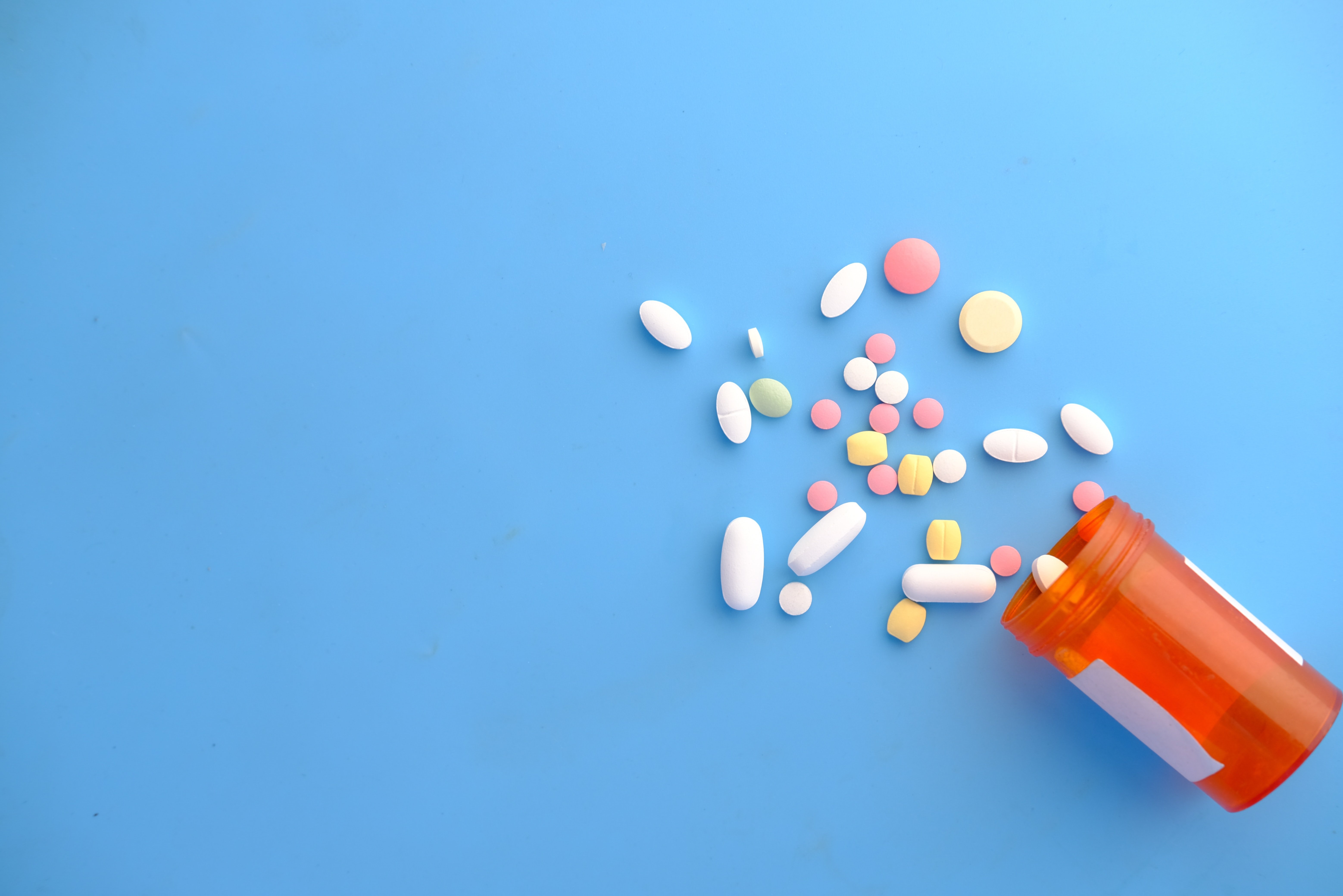 Different coloured pills spilling out of a medication jar on a blue background