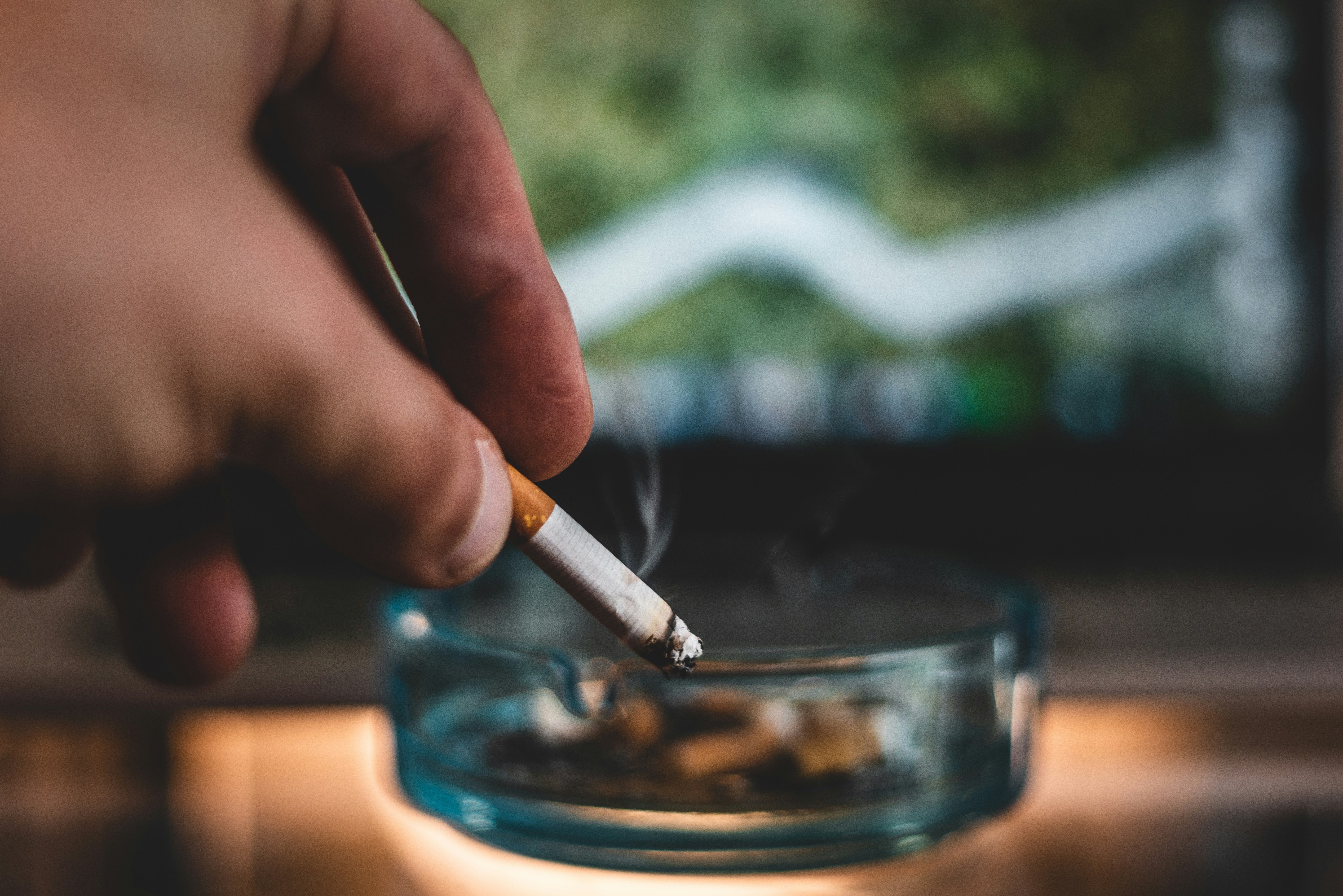 A hand holding a lit cigarette towards an ashtray